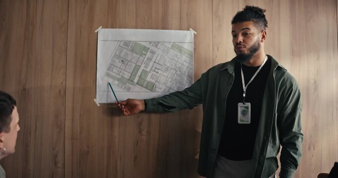 A man stands in an office and shows a map while talking to a small group of people