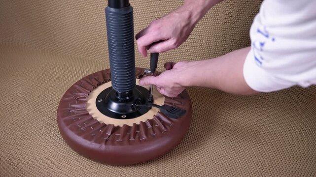 Handyman assembling office stool furniture with screwdriver. Professional furniture assembler screwing a metal plate to the bottom of a new office chair, completing the assembly process