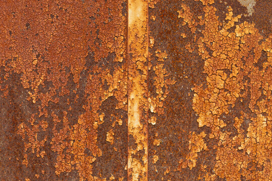 Textured close-up view of an old metal panel with extensive rust and flaking paint. The surface shows layered corrosion, varied orange and brown tones, and a