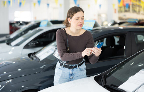 Young woman uses her smartphone to scan QR code on sticker on car window at car dealership