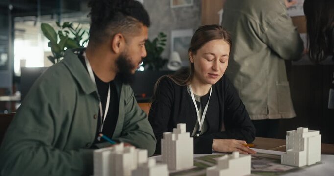 Two coworkers work together in an office, looking at plans and models while sharing ideas at a table in the afternoon