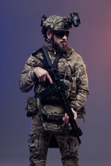 Fototapeta premium Male soldier in tactical camouflage uniform holds a rifle, equipped with night vision goggles and tactical gear, posed against a gradient background emphasizing military readiness