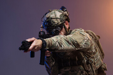 Obraz premium Armed soldier in tactical gear aims firearm with precision, wearing night vision goggles and camouflage uniform against a gradient background