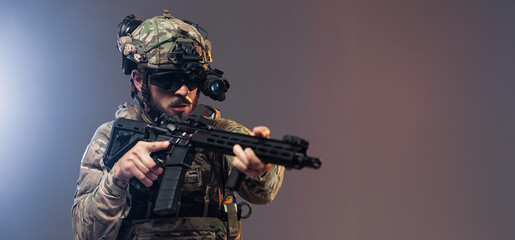 Obraz premium Male soldier in tactical gear aiming a rifle with night vision goggles, wearing camouflage uniform, set against a gradient background with dramatic lighting effects