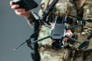 Military serviceman in camouflage uniform holding a remote-controlled drone in neutral indoor environment. Concept military technology, UAV systems and defense innovation.  © wedmoments.stock