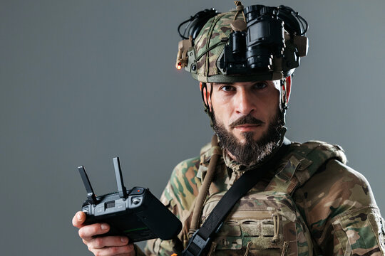 Military operator in camouflage uniform managing UAV drone and communication equipment via handheld controller in controlled studio setup. Concept reconnaissance, security and military systems.
