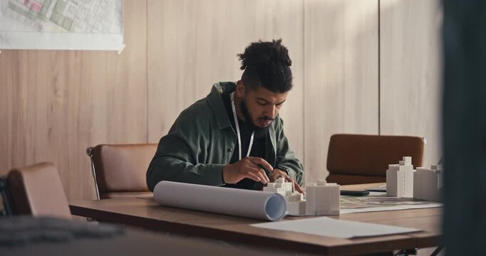 A man sits at a desk in an office. He writes notes and works on plans while focusing on his task
