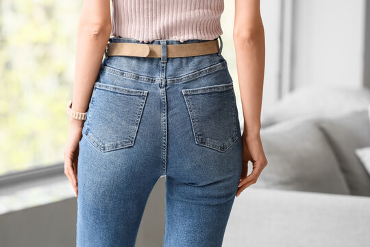 Young woman in stylish jeans at home, back view