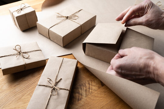 Woman wrapping Christmas gift box with kraft paper and handmade packaging