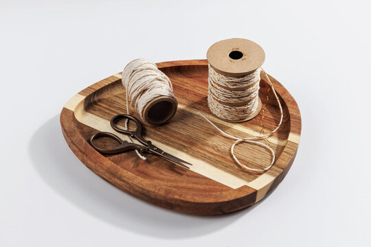 Cotton twine spool with decorative string and craft scissors arranged on wooden tray, rustic diy craft supplies and packaging materials concept