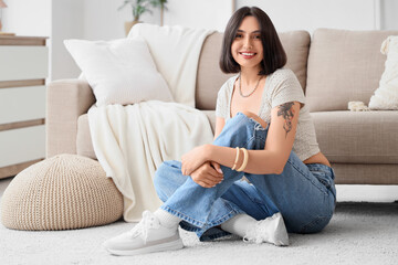 Fototapeta premium Smiling young woman sitting on floor in cozy living room, relaxing at home with casual style
