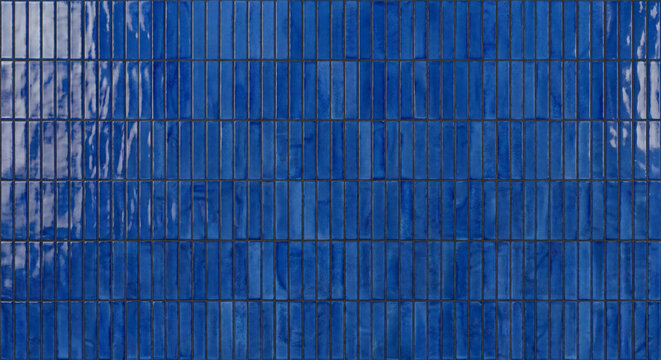 Full frame view of a vibrant blue ceramic tile wall texture background with small vertical brick shapes and glossy glazed surface reflections.