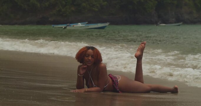 Slow-motion footage of a red-haired influencer wearing a breezy mini skirt and bikini top on a pristine tropical beach.
