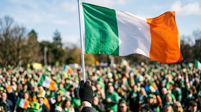 The Irish national flag waving in the wind with a crowd of people in the background during St. Patrick's Day.