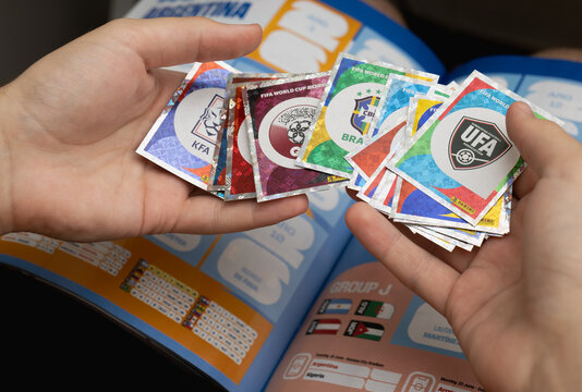 Hands holding shiny Panini football stickers over a collector album, featuring national football association badges for the 2026 World Cup tournament.
