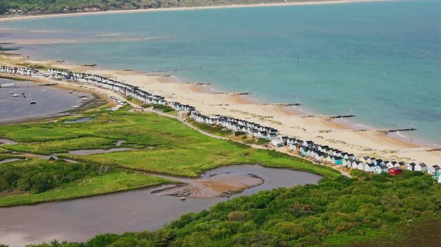 Drone footage looking across Mudeford Sandbank with beach huts sandy beach turquoise sea Christchurch Harbour wetlands and coastal landscape.