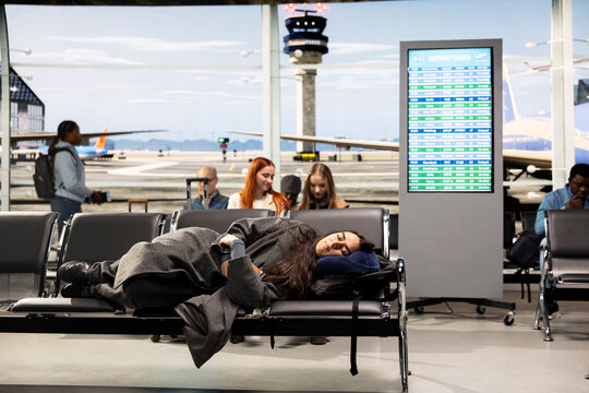 Tired woman sleeping on metal benches in airport international transport hub waiting area.