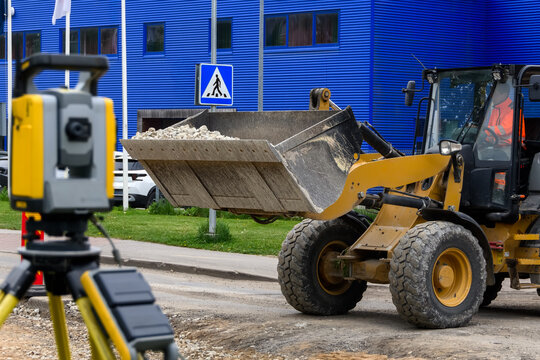 Wheel loader with crushed stone bucket and blurred total station at road construction site