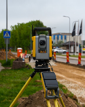 Total station theodolite on tripod at road construction site.