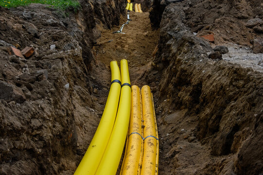 Yellow plastic corrugated pipes installed in an open earth trench at a construction site