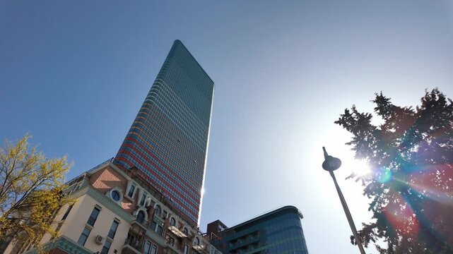 Modern skyscraper standing against a clear blue sky on a bright sunny day, with the sun moving and creating beautiful optical lens flares, showcasing contemporary urban architecture and design