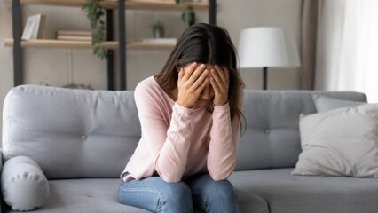Obraz premium Sad Depressed Woman Sitting on Sofa Covering Face During Emotional Crisis