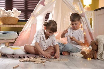 Little girl and boy playing with building blocks in wigwam at home © New Africa