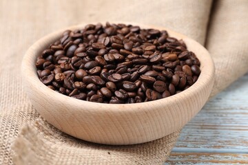 Fototapeta premium Aromatic coffee beans in bowl and burlap fabric on wooden table, closeup