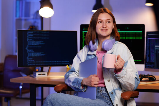 Happy female programmer with laptop, cup of coffee and computers working in office at night