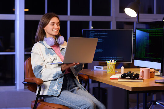 Happy female programmer with headphones, laptop and computers working in office at night