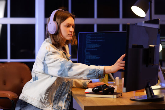 Female programmer with headphones and computers working in office at night