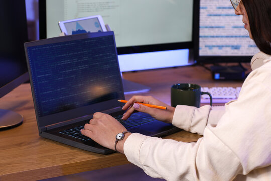 Young female programmer with cup of coffee and laptop working in modern office at night, closeup