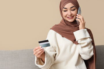 Muslim woman with credit card talking by mobile phone at home. Online banking concept