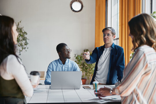 Diverse business professionals conducting a meeting at a table in a modern office, collaborating on a project, communicating ideas, and discussing important work topics