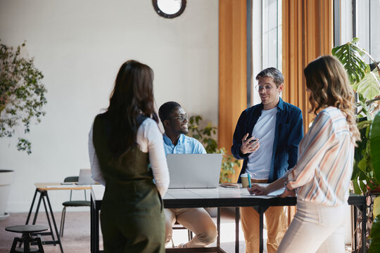 Diverse business professionals actively engaging in a collaborative conversation and sharing insights around a table in a bright, contemporary office environment
