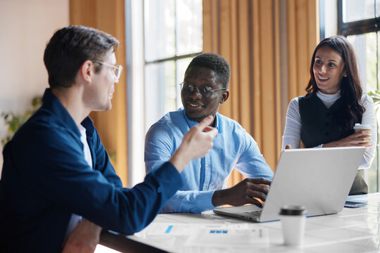 Diverse business professionals collaborating on a project in a modern office, discussing strategies and ideas during a productive team meeting, working together with a laptop