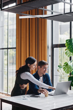 Professional colleagues collaborating on a laptop in a modern coworking space, focusing on planning new business strategies and working together