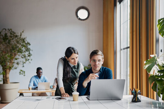 Business people collaborating on a laptop in a modern office, young male and female colleagues brainstorming ideas and working together on a new project, showing teamwork and consultation