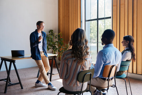 Young male leader presenting new ideas and strategy to diverse business team during creative collaboration session in modern startup office workspace