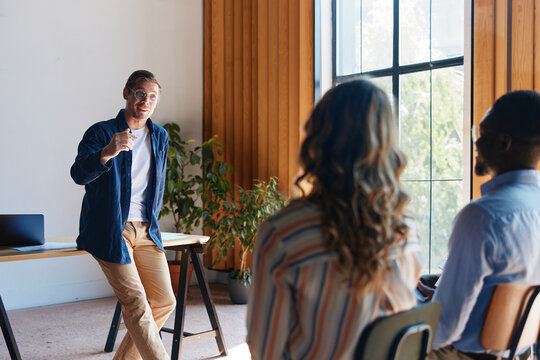 Professional man leading business presentation to diverse team in modern office, giving instruction and collaborating on project strategy
