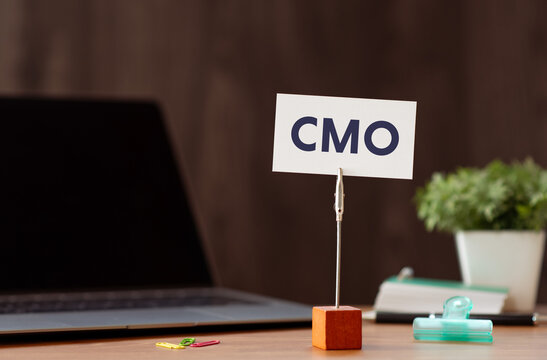 Eye-catching image of CMO text on card. The word stands for Chief Marketing Officer. Shown with laptop, clips.