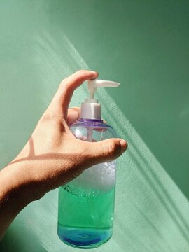 Hand holding green hand sanitizer bottle.