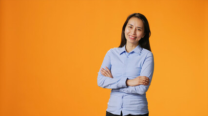 Fototapeta premium Portrait of positive model with arms crossed posing on camera over background, smiling with confidence in studio, cheerful satisfied woman with joyful expression enjoying glamour shoot