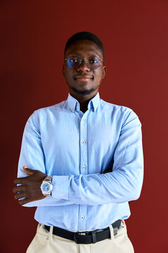 Young black man in professional blue shirt and glasses standing confidently with crossed arms, portraying a successful and intelligent business professional