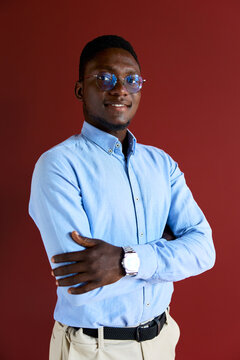 Confident black businessman standing with crossed arms, smiling at camera, wearing glasses and a light blue shirt, representing professionalism and success in a corporate environment