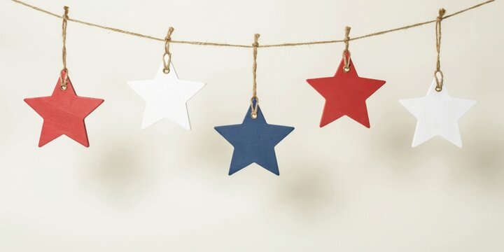 Stars made of painted wood hang from a thin string against a neutral wall to represent a patriotic or holiday display.