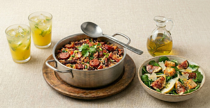 arroz carreteiro acompanhado de salada de agri&atilde;o e r&uacute;cula, figo grelhado, fatias de pera e parmes&atilde;o e um suco de abacaxi com hortel&atilde; sobre mesa posta