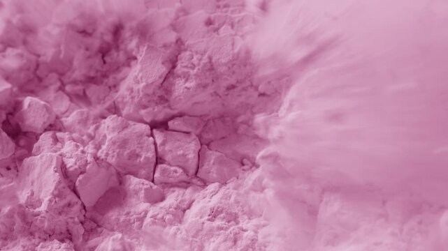 Extreme macro slow-motion shot of crumbled pink powder surface being blown with air stream, breaking its structure and chipping it into small pieces