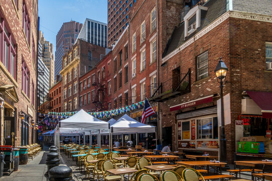 New York, NY - US - Jun 5, 2026 Historic Stone Street in Lower Manhattan features bustling outdoor patio dining, charming brick buildings, festive hanging banners, and towering city skyscrapers.