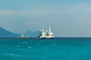 Obraz premium Croatian twin fishing trawlers preparing for a catch in clear turquoise waters near the Peljesac peninsula with lighthouse on the background, Croatia